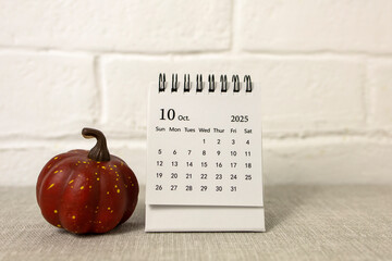 A desktop calendar for October 2025 and a pumpkin on the table. Halloween is coming soon.