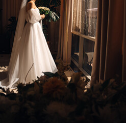 without a face. A bride in a lush white dress in the hotel room by the window