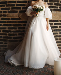 without a face. A bride in a lush white dress against a brick wall.