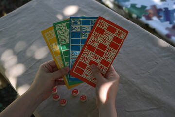 Lotto game. Outdoors at the table, colorful cards with numbers in the hands of a girl and playing barrels nearby