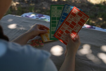 Lotto game. Outdoors at the table, colorful cards with numbers in the hands of a girl and playing barrels nearby