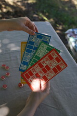 Lotto game. Outdoors at the table, colorful cards with numbers in the hands of a girl and playing barrels nearby