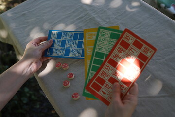 Lotto game. Outdoors at the table, colorful cards with numbers in the hands of a girl and playing barrels nearby