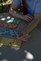 Lotto game. Outdoors at the table, colorful cards with numbers in the hands of a girl and playing barrels nearby