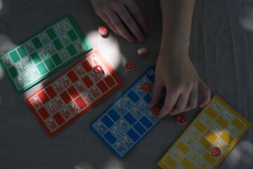 Lotto game. Outdoors at the table, colorful cards with numbers in the hands of a girl and playing barrels nearby