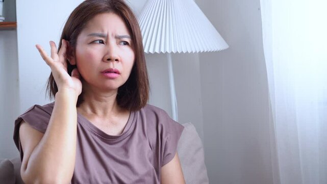 Asian woman hearing strange voices in her head, showing signs of auditory hallucinations possibly caused by mental health disorders, drug reactions, or early symptoms of schizophrenia