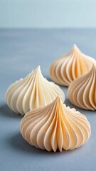 A close up view of four delicate meringue cookies with swirled textures arranged on a soft blue surface