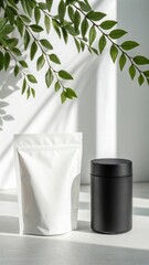 Minimalist product display featuring a white pouch and a black container with natural green foliage and soft shadow effects