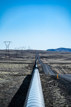 View of a silvery pipeline stretching across the arid landscape, paralleling a road under a clear blue sky, Nesjavellir, Gr&Atilde;&shy;msnes- og Grafningshreppur, Iceland.