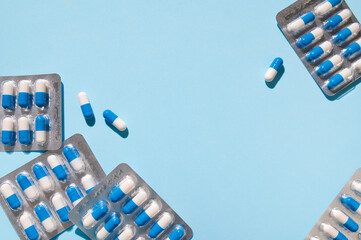 Health and medicine concept. White and blue capsules in silver blister pack on blue background top view. Tablets, pills, vitamins, food supplements, probiotic. Pharmacology, health and beauty care