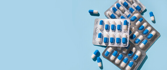 Health and medicine concept. White and blue capsules in silver blister pack on blue background top view. Tablets, pills, vitamins, food supplements, probiotic. Pharmacology, health and beauty care
