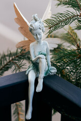 Peaceful fairy sculpture sitting on railing with pine branches in soft natural light