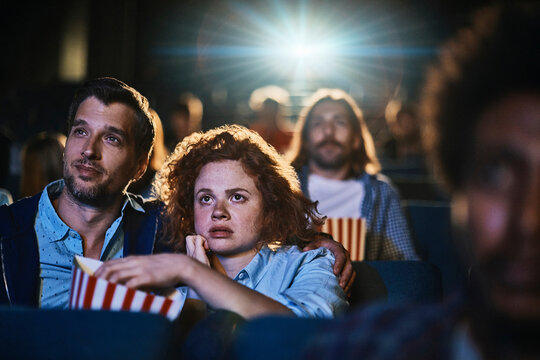 Young couple watching a movie and eating popcorn in a movie theater