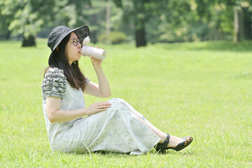 芝生に座って水筒の水を飲む若い日本人女性