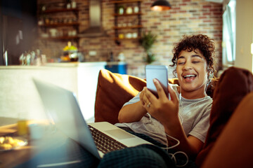 Happy woman listening to music with earphones on phone while relaxing at home