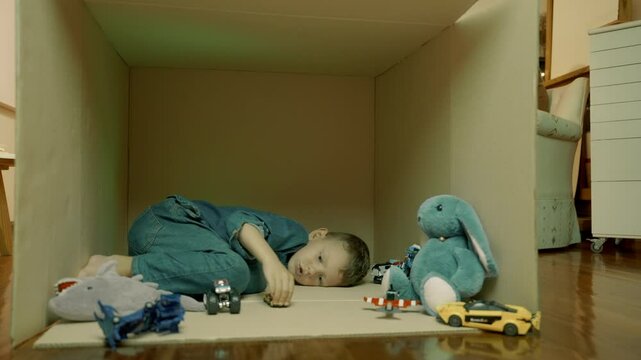Boy with toys in cardboard box deprived of adult attention. Cardboard box as symbol of his world