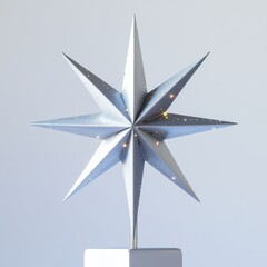 Fototapeta premium Shiny silver eight-pointed star ornament with subtle sparkles, mounted on a white base against a plain light background.