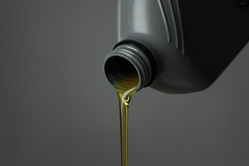 Pouring motor oil from canister on grey background, closeup. Space for text