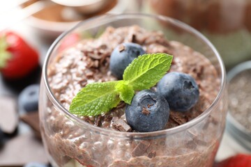 Delicious chocolate pudding with chia seeds and blueberries in glass on table, closeup