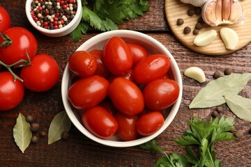 Tasty pickled tomatoes in bowl and ingredients on wooden table, flat lay