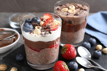 Delicious chocolate puddings with chia seeds, nuts and berries in glasses on grey table, closeup