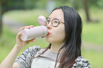 屋外でマイボトルに入れた水を飲む若い日本人女性