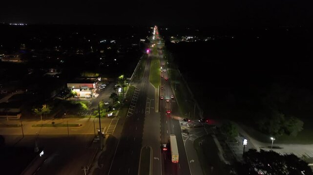 Aerial Birds Eye shot of traffic scene on main road of Brandon town. Night scene with trucks and cars in Florida. Lighting lantern, shops and restaurants along suburb intersection.