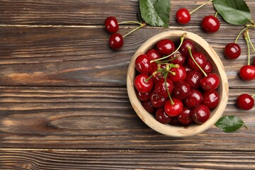 Fresh wet cherries in bowl and leaves on wooden table, flat lay. Space for text