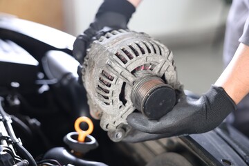 Auto part. Professional mechanic with alternator near open hood of car indoors, closeup