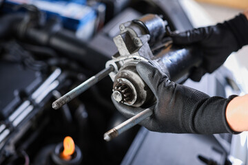 Auto part. Professional mechanic with starter motor near open hood of car indoors, closeup