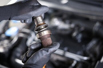 Auto part. Professional mechanic with drive shaft near open hood of car indoors, closeup. Space for...