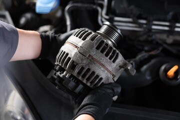 Naklejka premium Auto part. Professional mechanic with alternator near open hood of car indoors, above view