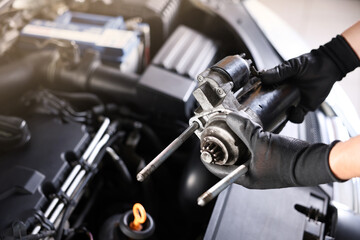 Auto part. Professional mechanic with starter motor near open hood of car indoors, closeup