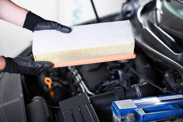 Auto part. Professional mechanic with air filter near open hood of car indoors, closeup