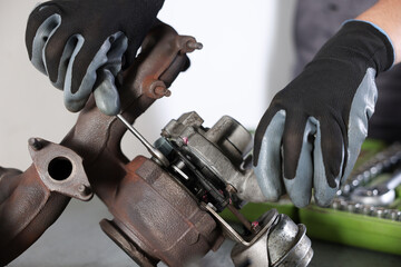 Auto parts. Professional mechanic with wrench fixing turbocharger at table indoors, closeup
