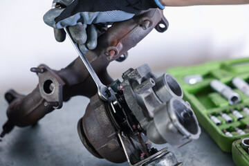 Auto parts. Professional mechanic with wrench fixing turbocharger at grey table indoors, closeup