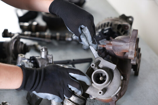 Auto parts. Professional mechanic with wrench fixing turbocharger at grey table indoors, above view