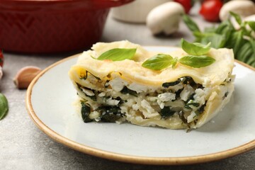 Piece of tasty vegetarian lasagna and ingredients on grey table, closeup