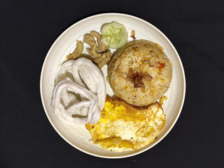 Fried rice served with sunny side up egg and fresh cucumber slices on a white plate, looks very delicious.