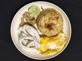 Fried rice served with sunny side up egg and fresh cucumber slices on a white plate, looks very delicious.