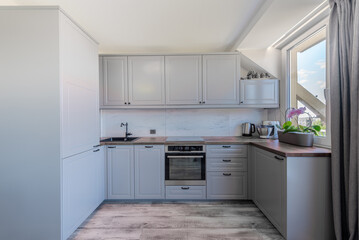 Fototapeta premium Modern Bright Grey Kitchen Interior with Wood Details and Large Window View