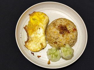 Fried rice served with sunny side up egg and fresh cucumber slices on a white plate, looks very delicious.