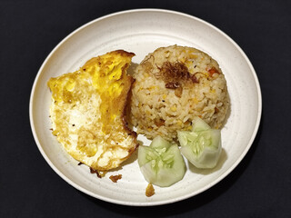 Fried rice served with sunny side up egg and fresh cucumber slices on a white plate, looks very delicious.