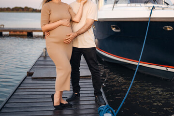 A man gently hugs a pregnant woman on the pier.