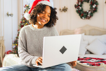 Merry Christmas. African woman in Santa hat having video chat in laptop. Blogger in festive mood recording video in social network. Girl having video call with friends family celebrating Christmas