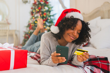 African American woman shopping online holding smartphone paying with gold credit card for Christmas gifts. Girl buying on Internet enter credit card details enjoying Christmas winter holidays at home