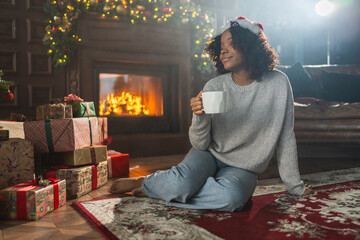 Merry Christmas. African American woman in Santa hat with cup of hot drink coffee tea near...