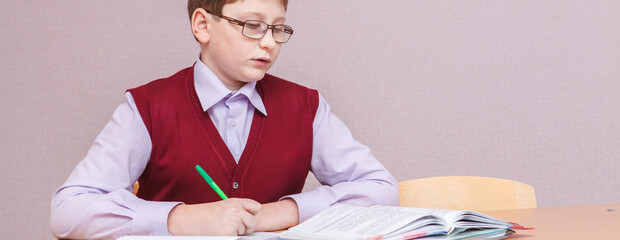 boy with glasses sitting at a desk writing. in glasses and school uniform