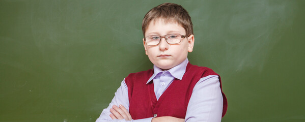 boy standing with his arms crossed at a school board. in glasses and school uniform