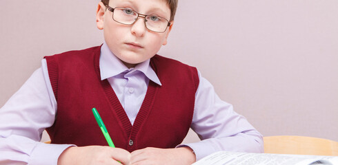 boy with glasses sitting at a desk writing. in glasses and school uniform